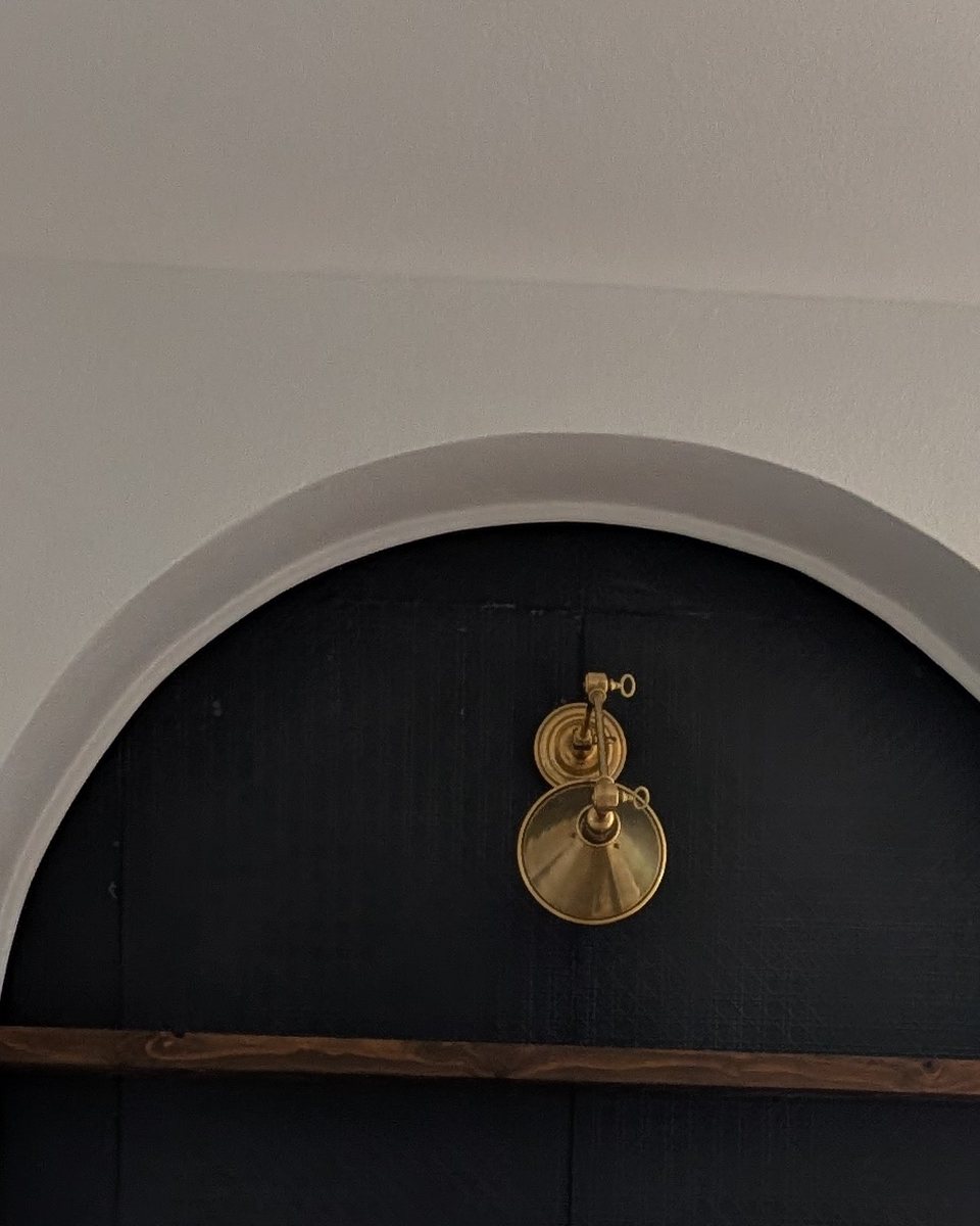 The completed arch, plastered and painted, with a brass sconce and walnut shelf